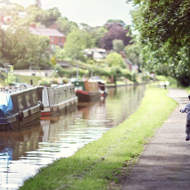 boy riding his bike alongside canals with narrowboat moored